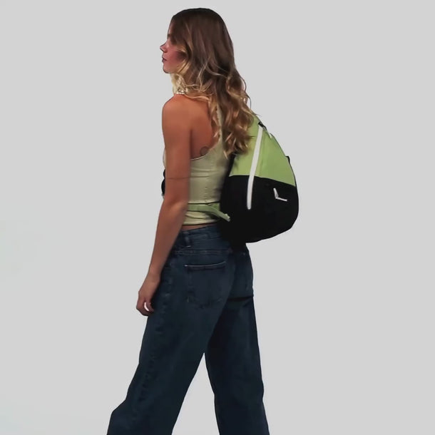 A woman shows features of the Sherpani Esprit Palm Green Sling Bag, such as the phone pocket on the strap. 