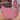 A woman packs a water bottle into the Sherpani Mina Desert Pink Medium Crossbody Bag water bottle pocket. 